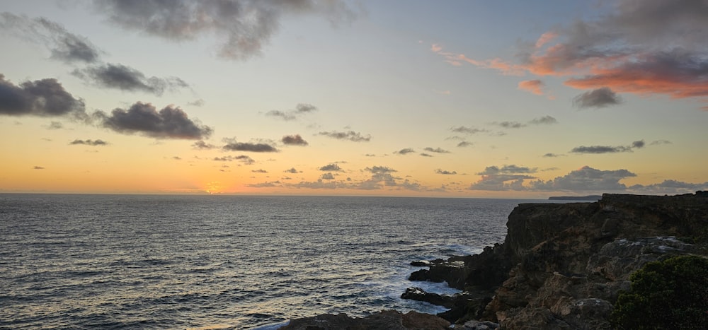 the sun is setting over the ocean on a rocky cliff