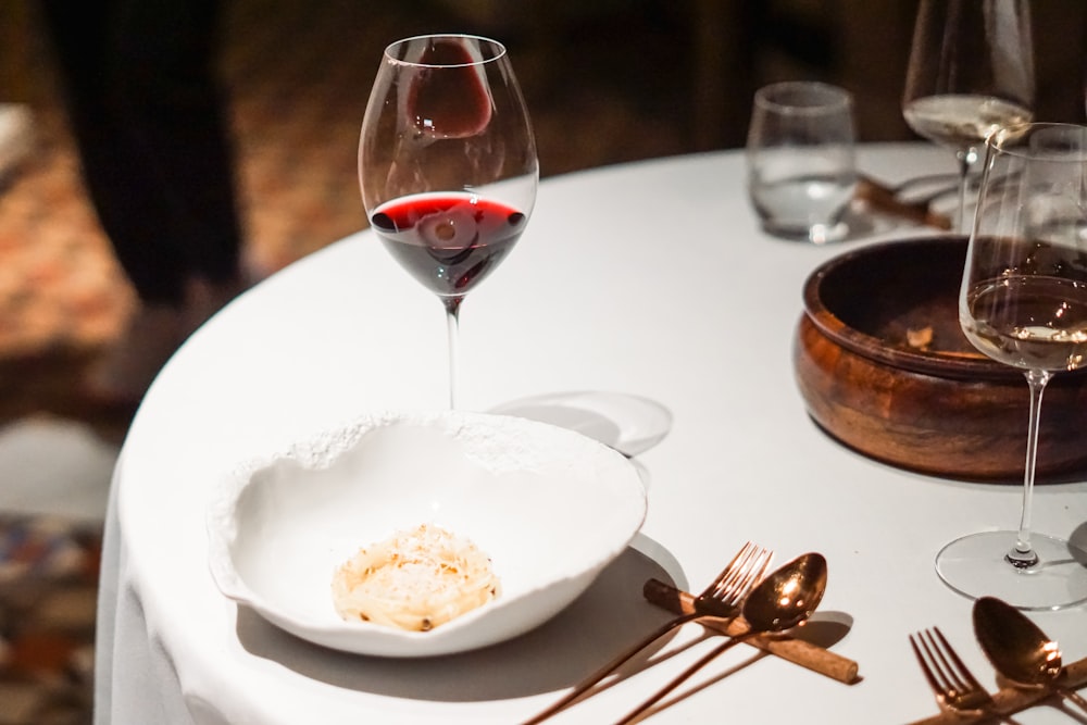 a white table topped with a bowl of food and a glass of wine