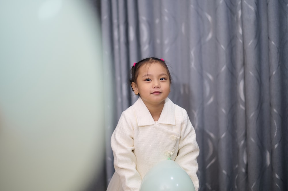 a little girl holding a balloon in front of a curtain
