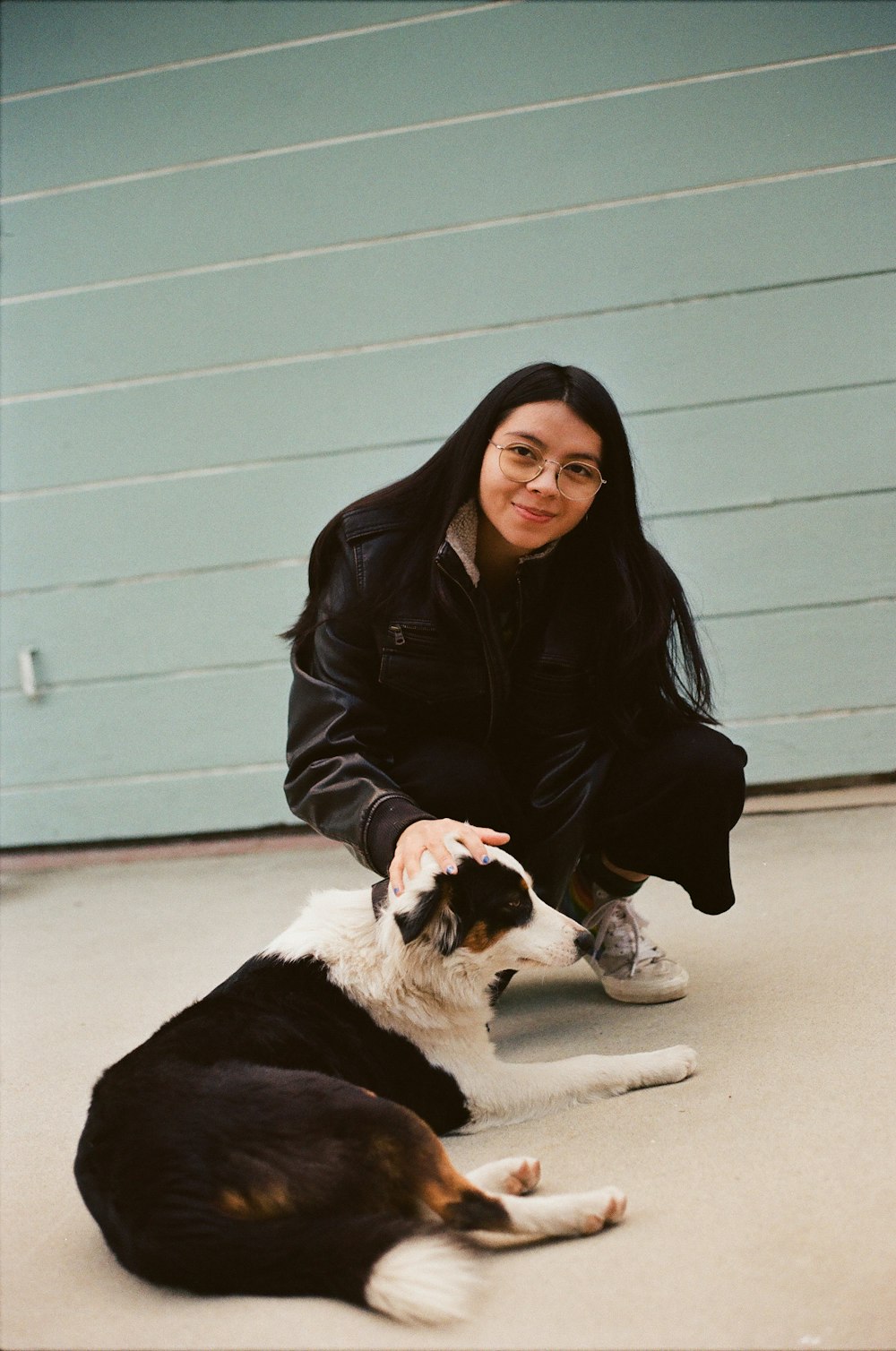 a woman kneeling down next to a black and white dog