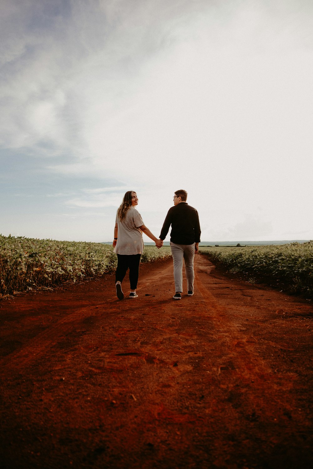 ein Mann und eine Frau, die Händchen halten, gehen einen Feldweg entlang