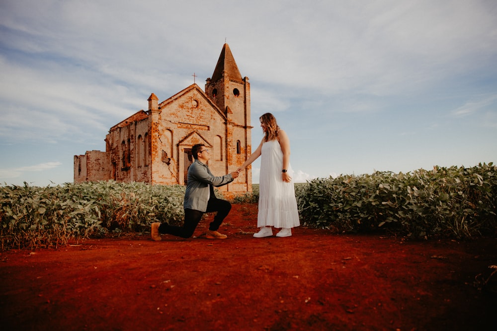 a man kneeling down next to a woman in front of a church