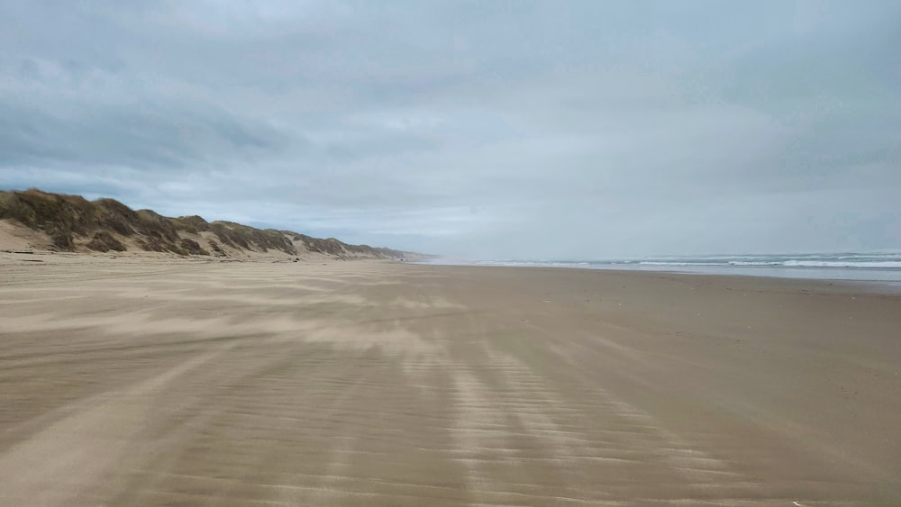 a sandy beach next to the ocean under a cloudy sky