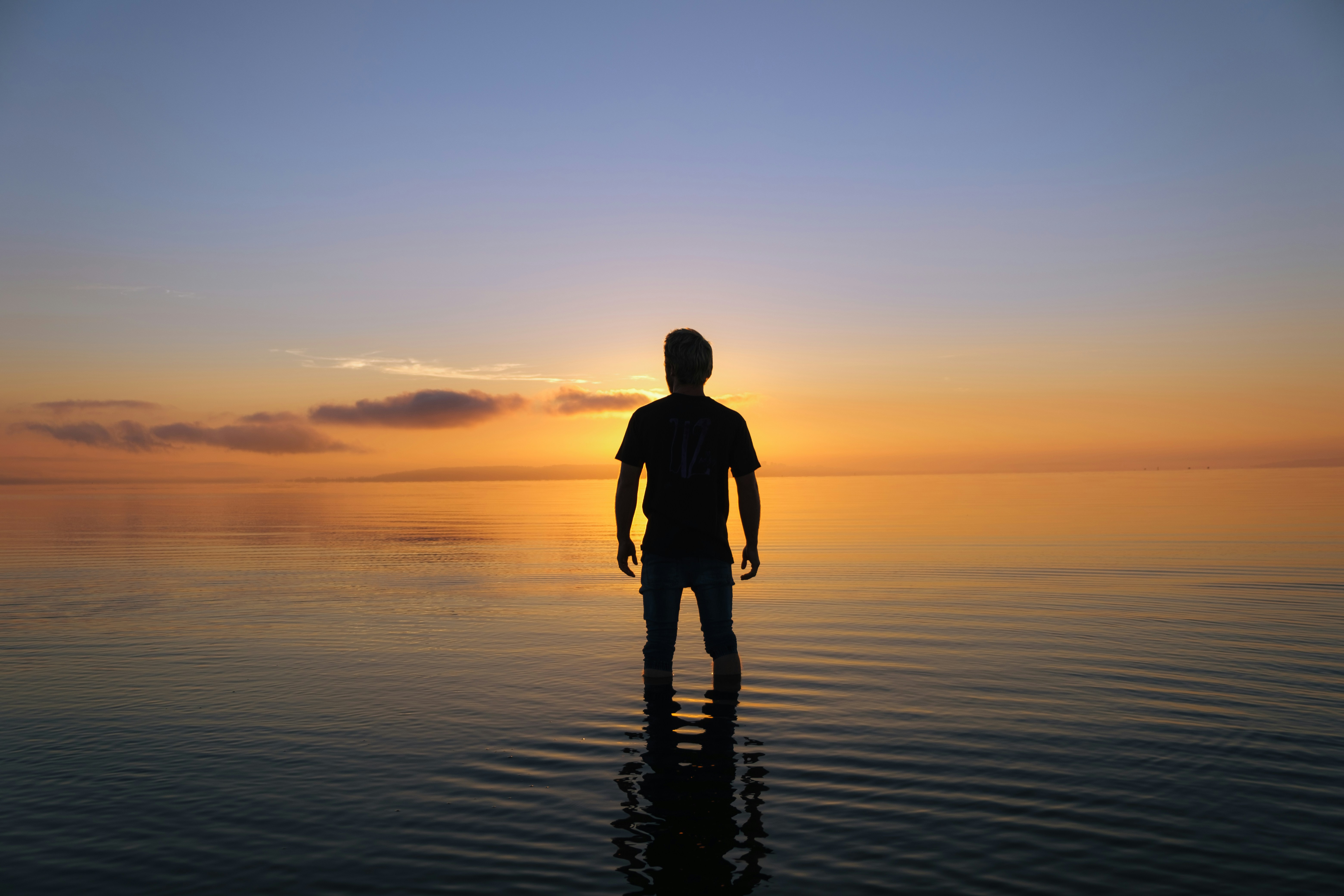 a man standing in the water at sunset, Man looking at sunrise over ocean