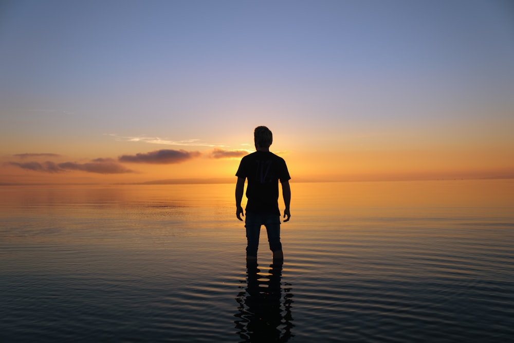 a man standing in the water at sunset