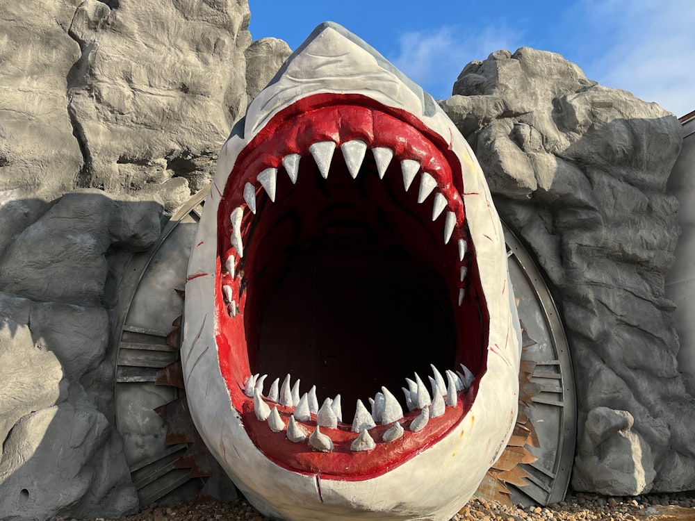 a fake shark with its mouth open in front of a rock wall