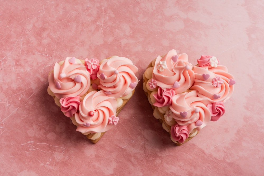 two heart shaped cupcakes on a pink surface