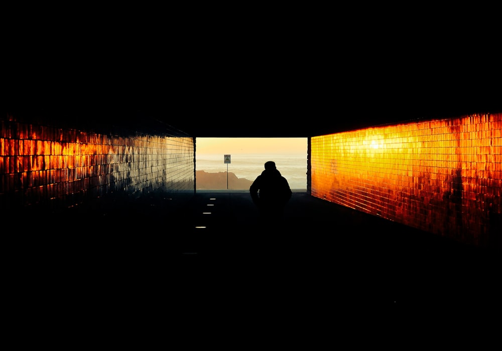 a person standing in a dark tunnel with the sun shining through