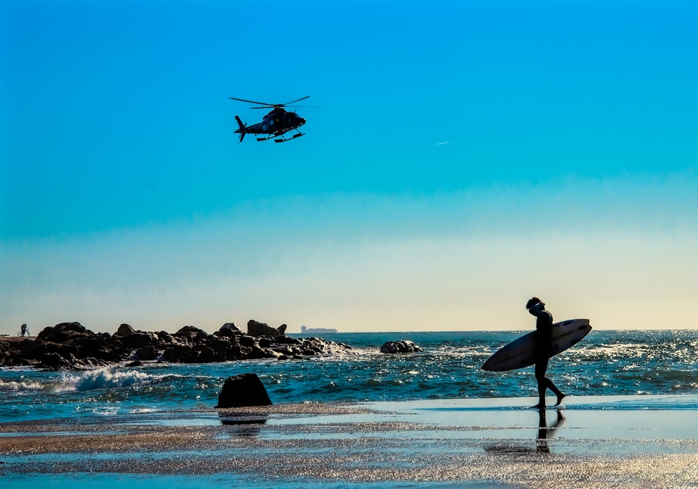 a man holding a surfboard while flying a helicopter