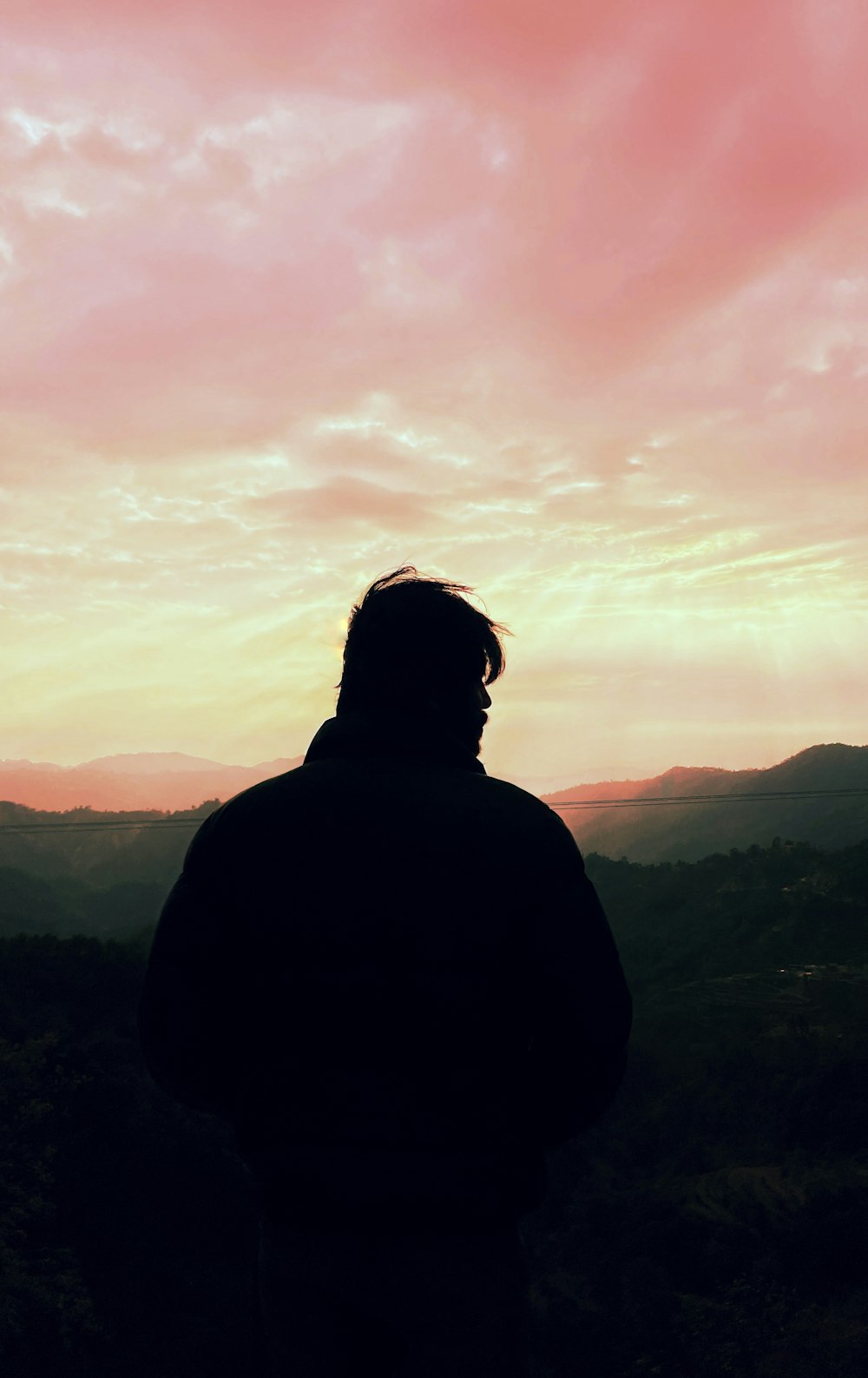 a man standing on top of a hill under a pink sky
