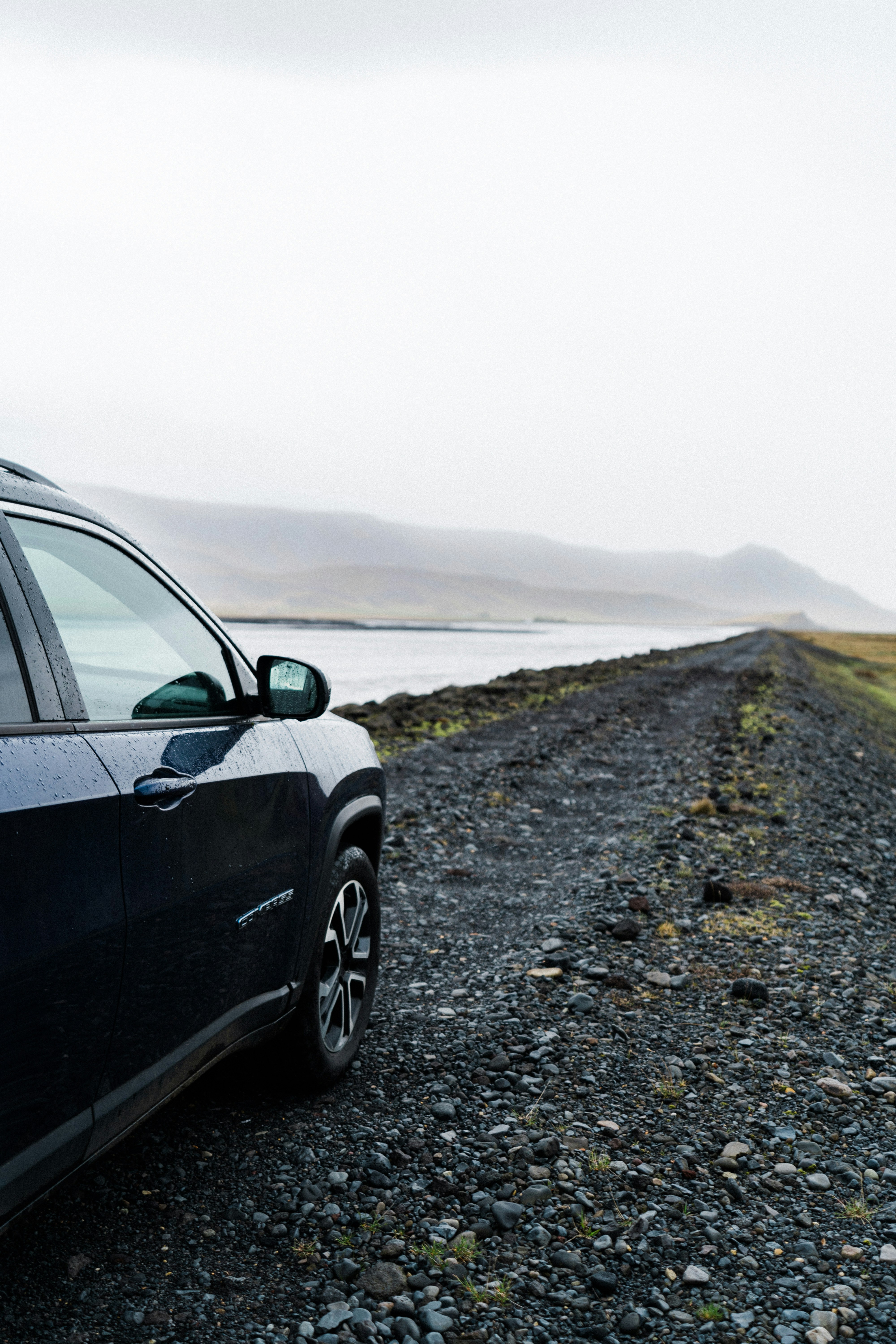 a car parked on a gravel road next to a body of water