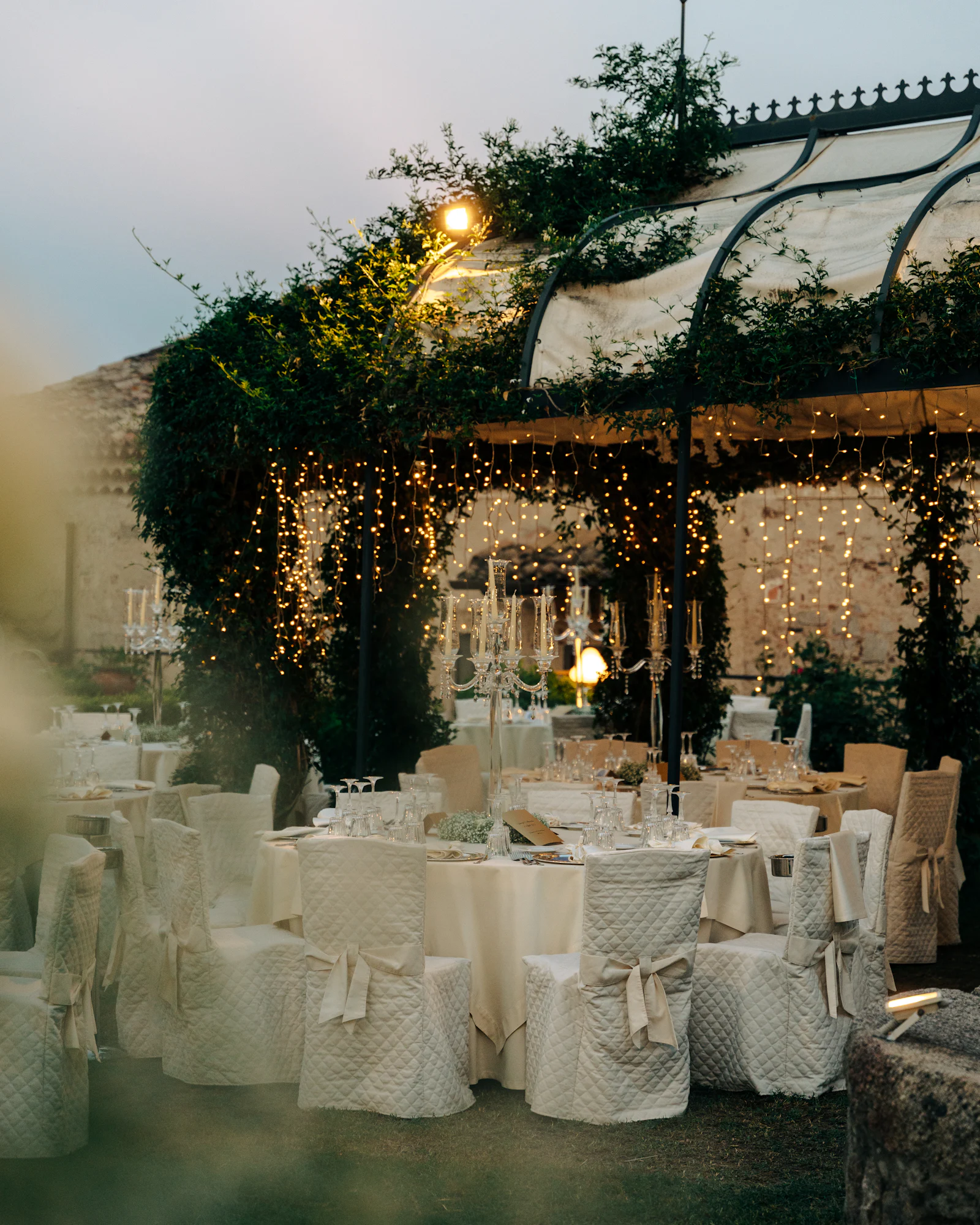 Long tables in white linen set out under trees.