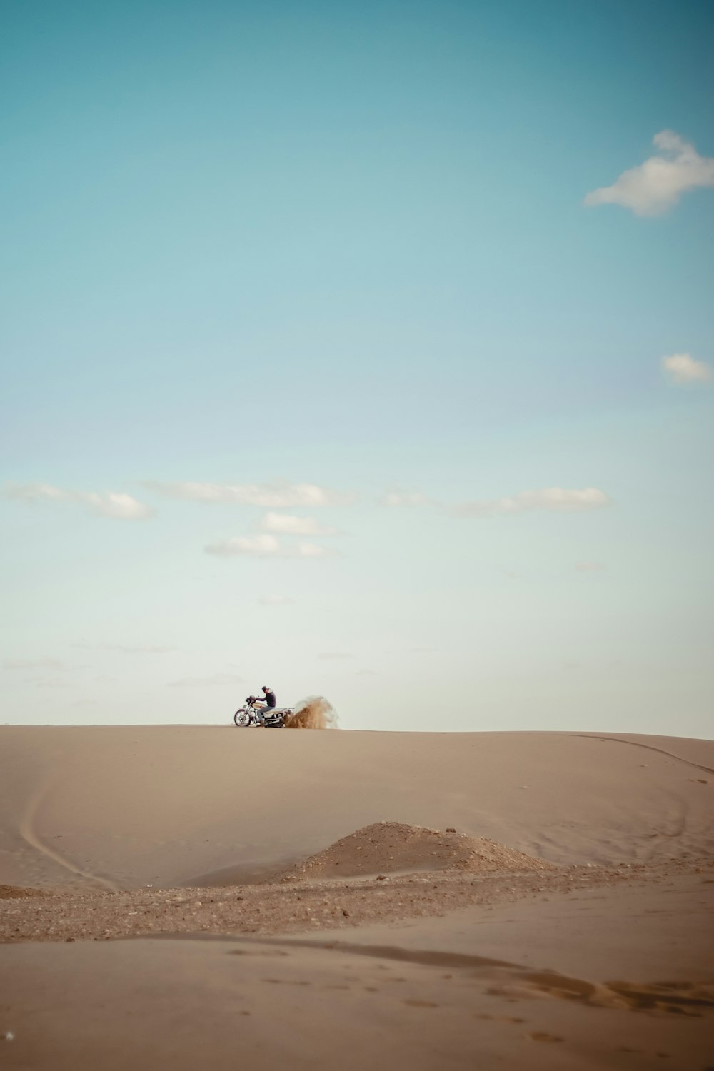 a person riding a motorcycle on top of a sandy hill