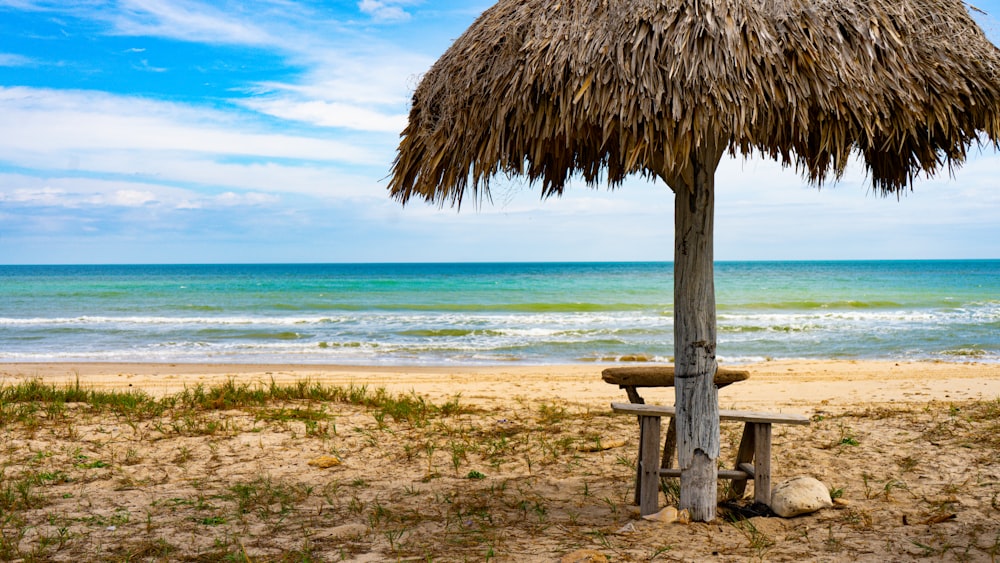 a wooden bench under a straw umbrella on a beach