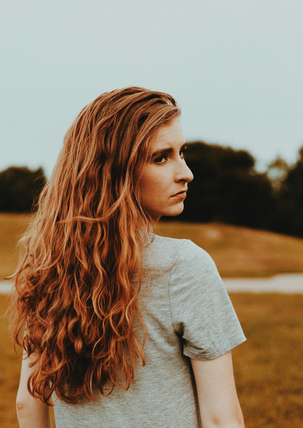 a woman with long red hair standing in a field