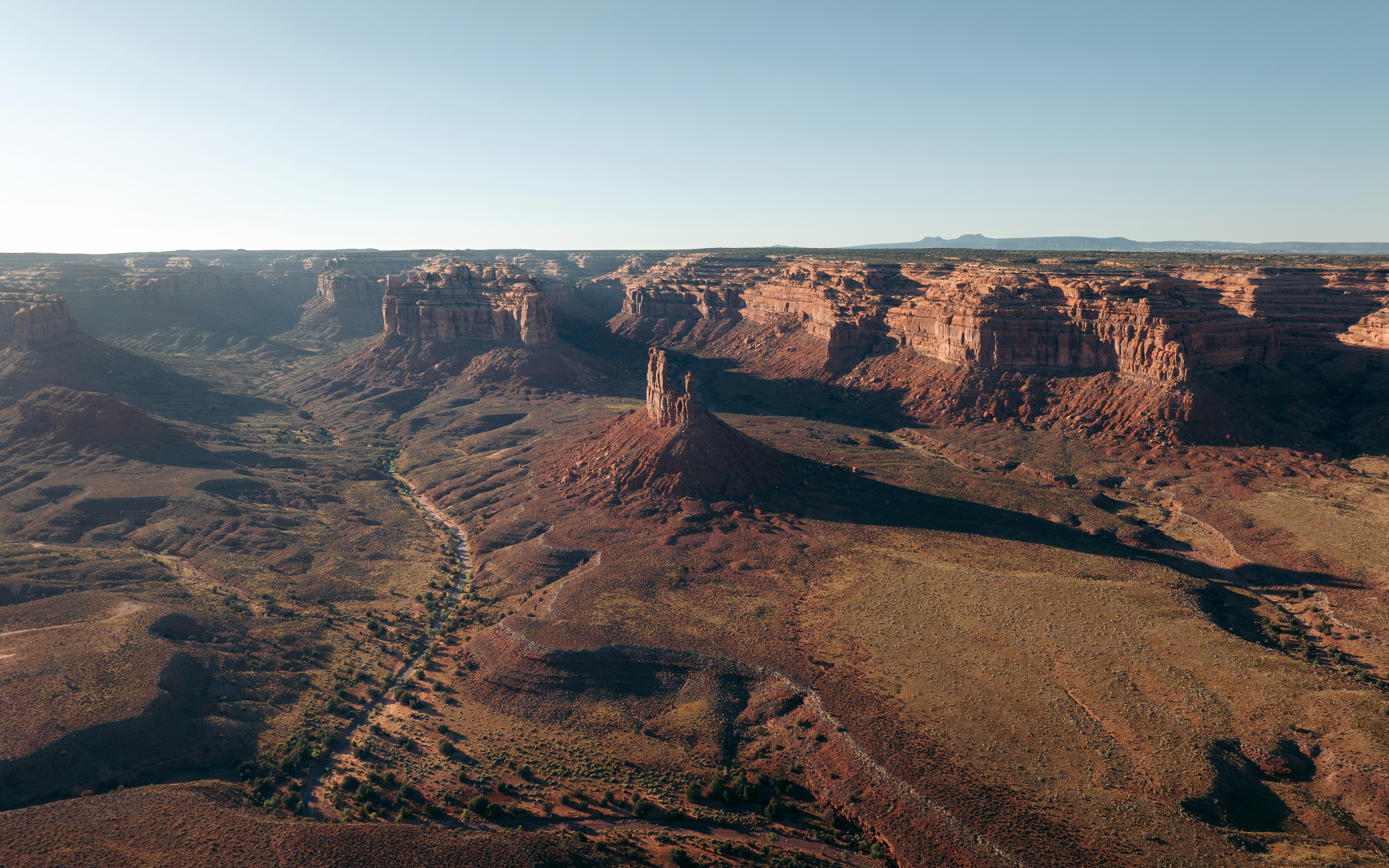 Vast desert scenes of sprawling orange stone monuments in the deserts of Utah. A small oasis of a dry riverbed flows through the earth, providing a small glimpse of life.