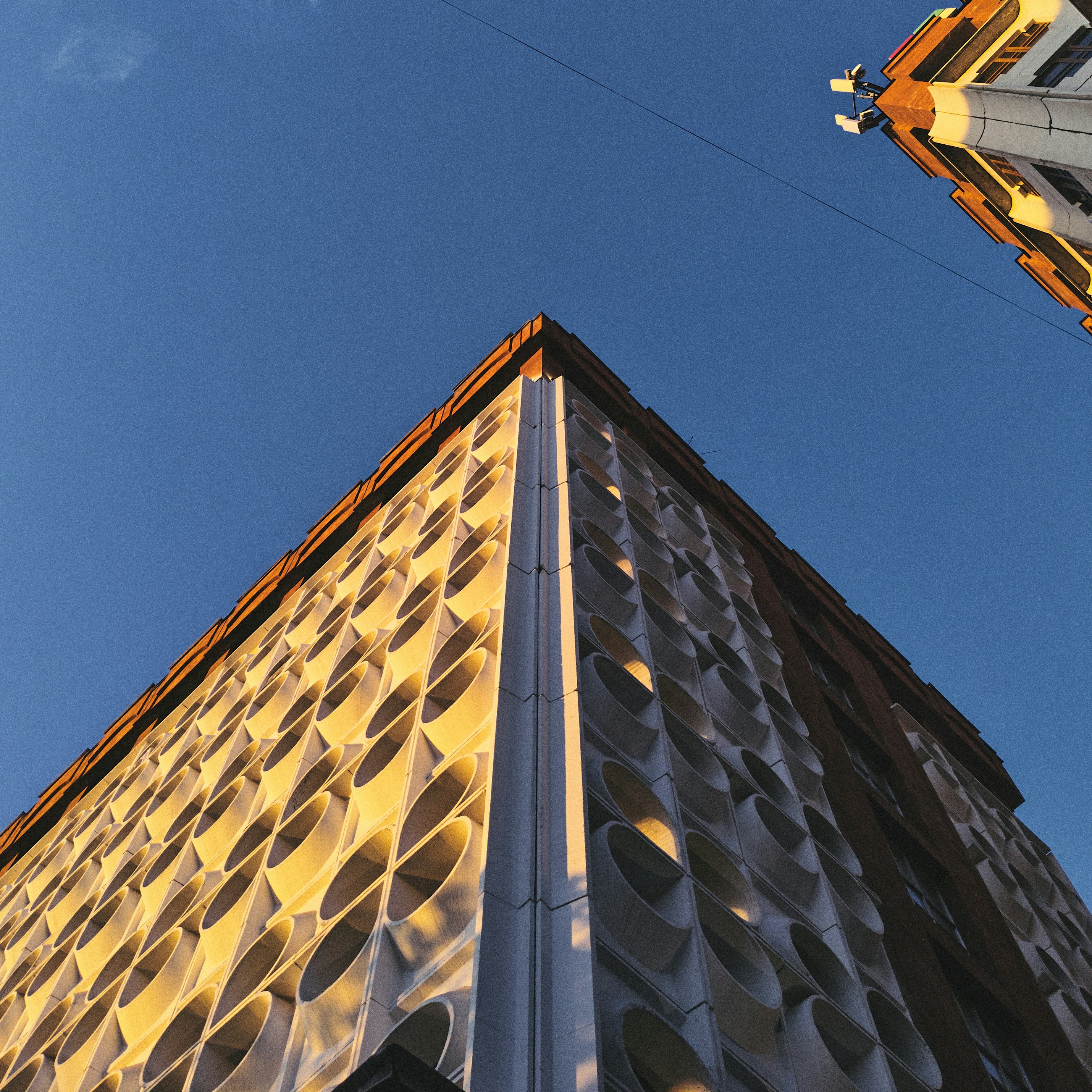 Dramatic high-rise residential tower with geometric facade pattern, golden hour light, deep blue sky background