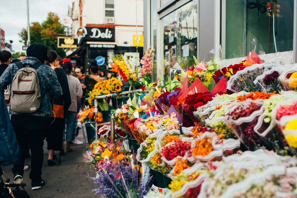 a group of people walking down a street next to a bunch of flowers