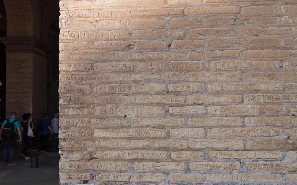 a group of people walking down a sidewalk next to a brick wall