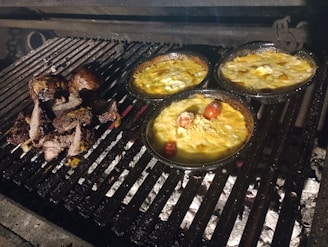 a bbq grill with four pans of food cooking on it