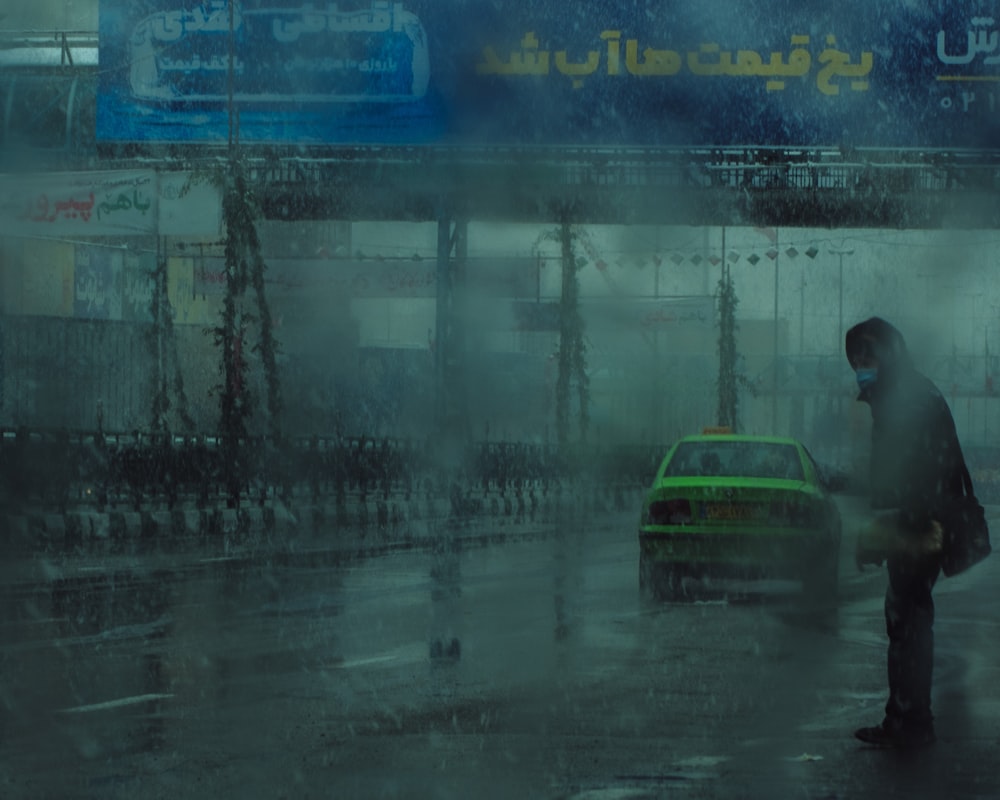 a man standing in the rain next to a green car