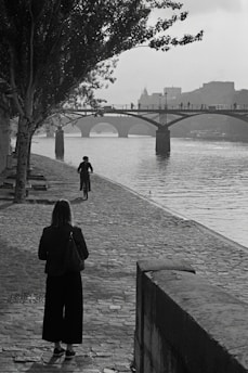 a woman walking down a sidewalk next to a river