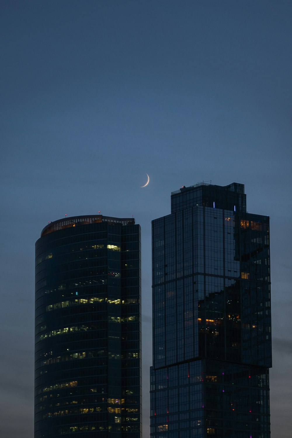 two skyscrapers at night with the moon in the sky