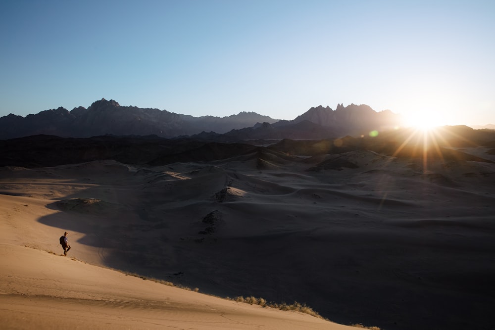 uma pessoa está andando no deserto ao pôr do sol