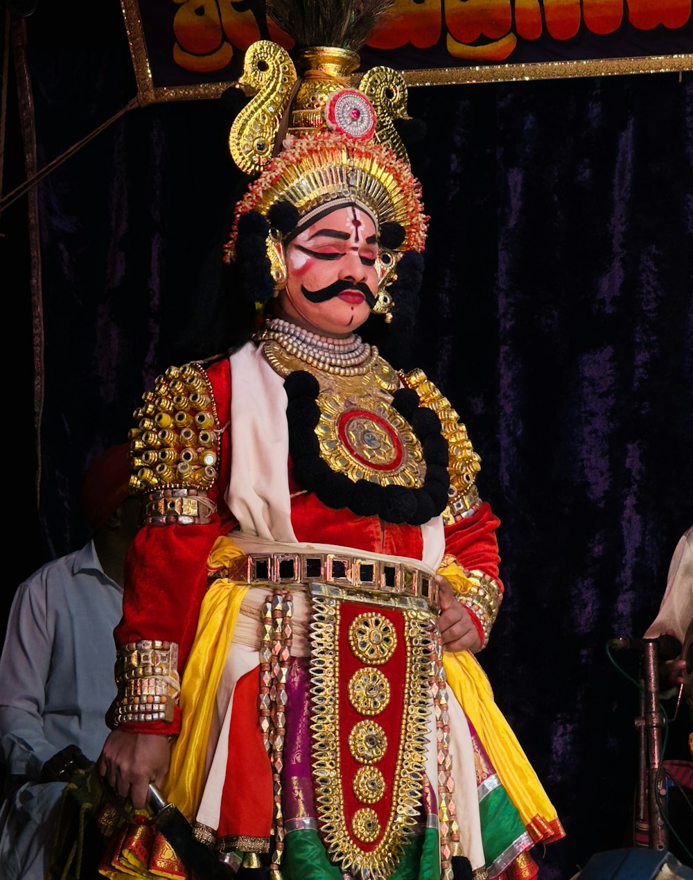 Ein Mann in einem bunten Kostüm steht vor einer Bühne