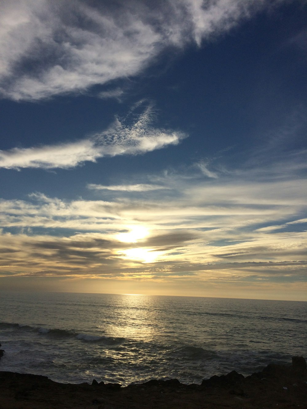 the sun is setting over the ocean on a cloudy day