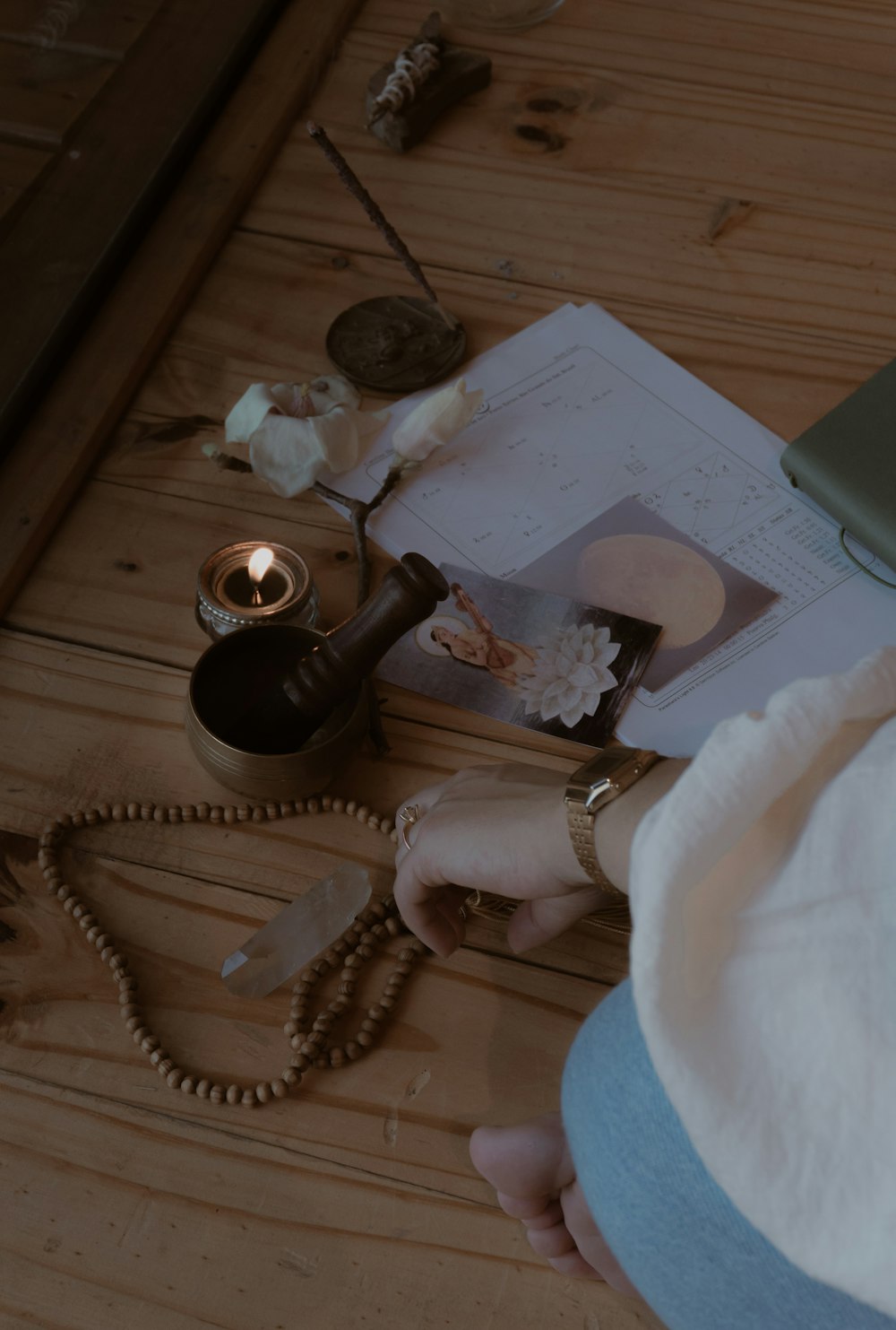 a table with a candle, a book, a necklace, and a cell phone