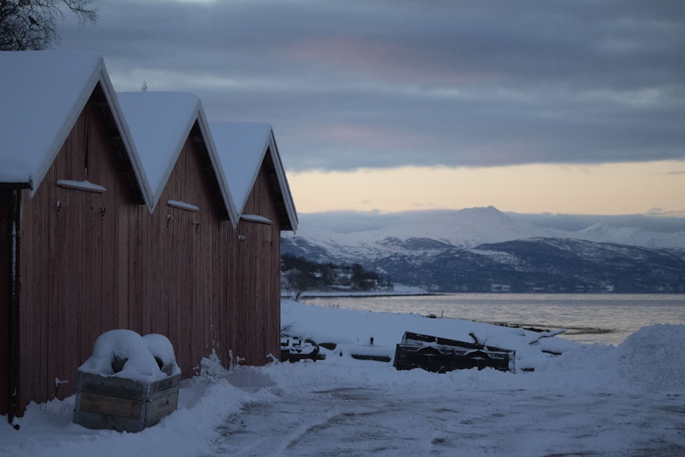 a wooden building with snow on the ground and a body of water in the background