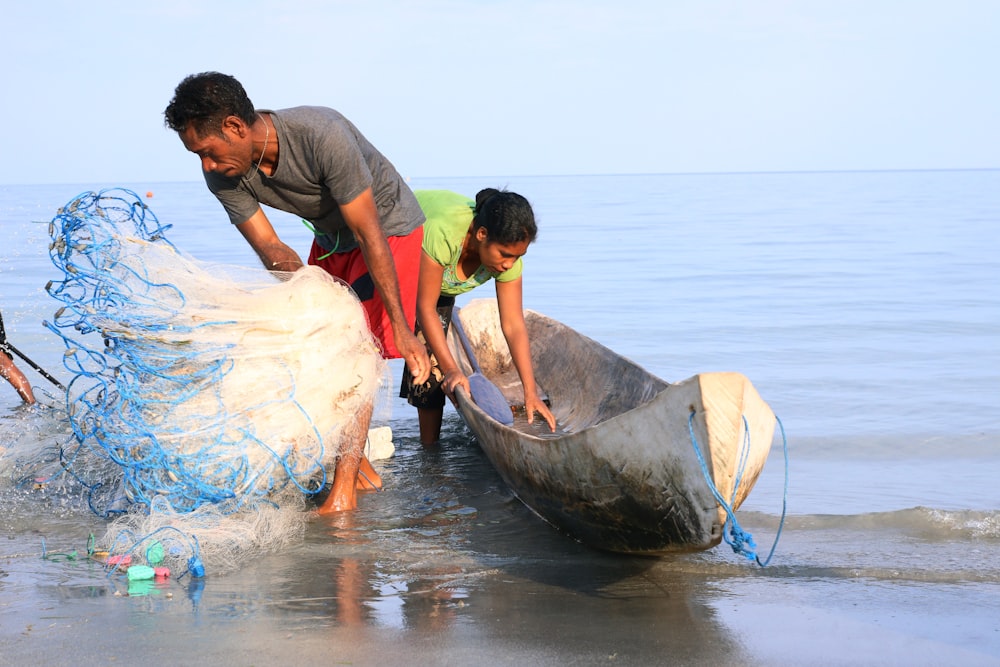 a man and a woman are pulling a boat out of the water