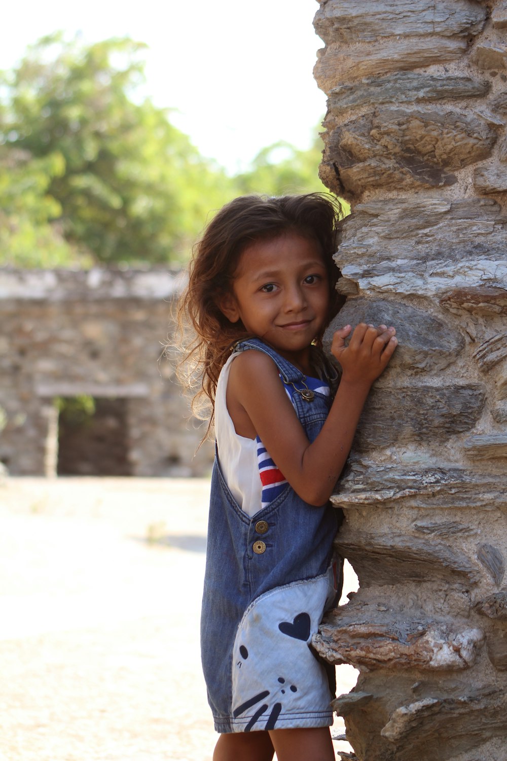 a little girl leaning against a stone wall