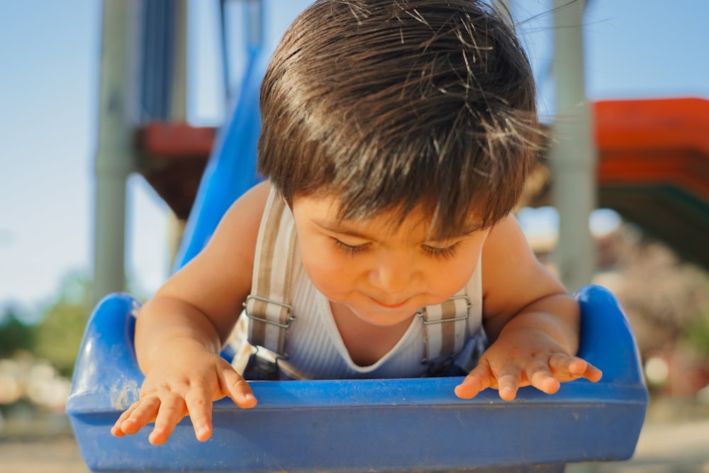 a little boy is playing in a blue slide