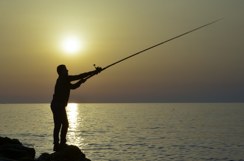 a man standing on a rock while holding a fishing rod
