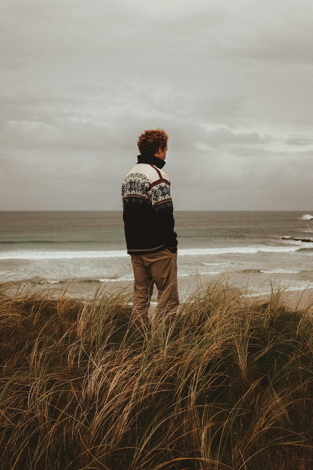 a man standing on top of a grass covered beach