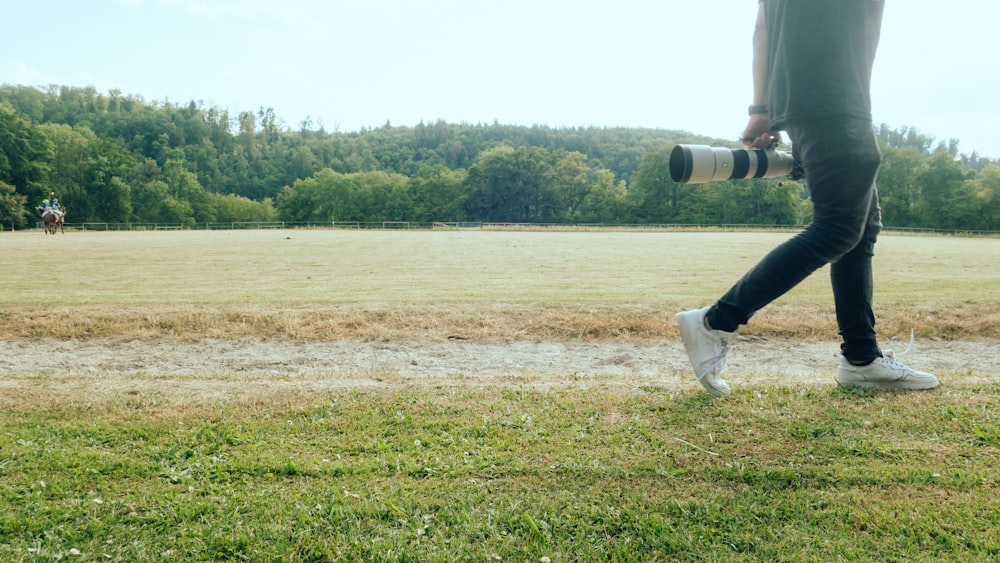 a man walking across a lush green field holding a camera