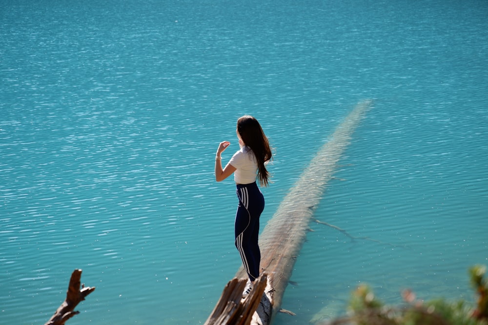a woman standing on a wooden dock next to a body of water