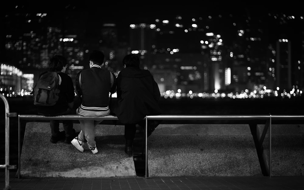 three people sitting on a bench in a city at night