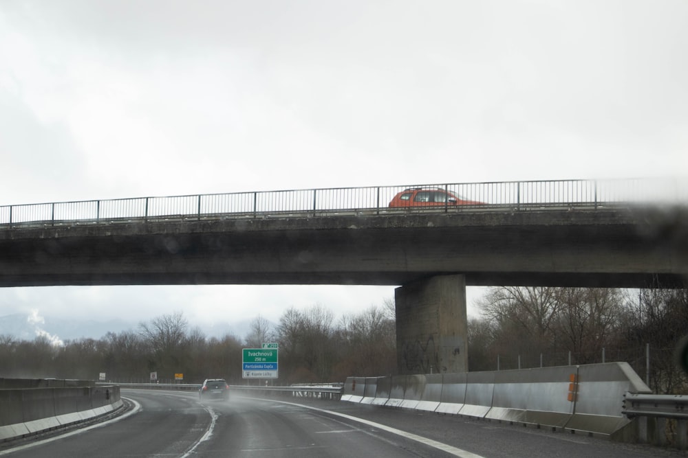 a red car driving on a highway under a bridge