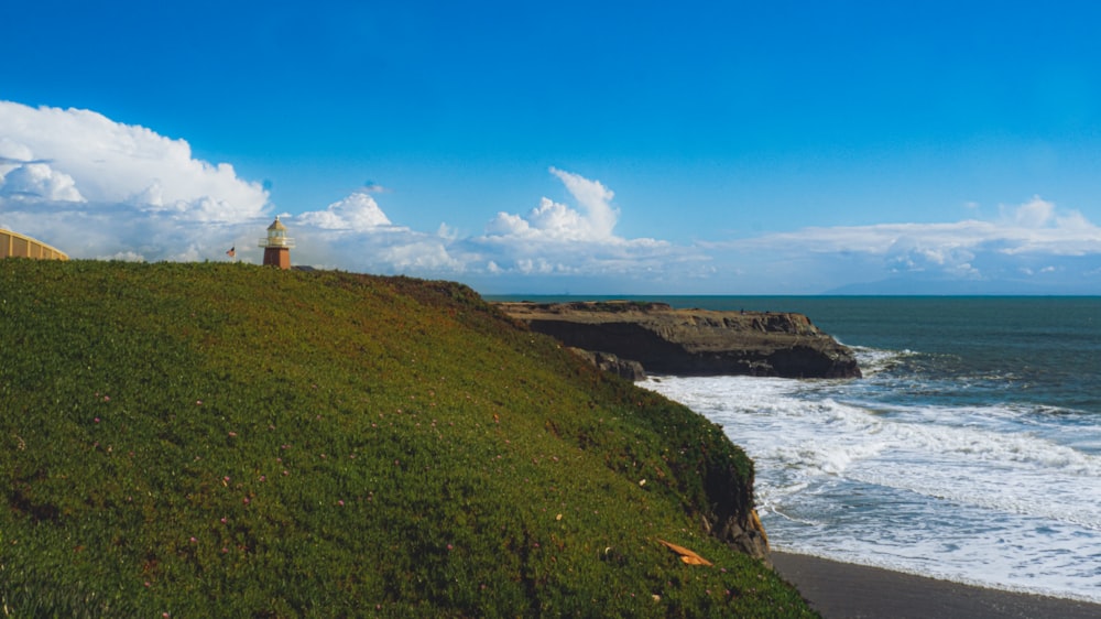 a grassy hill next to the ocean with a light house on top