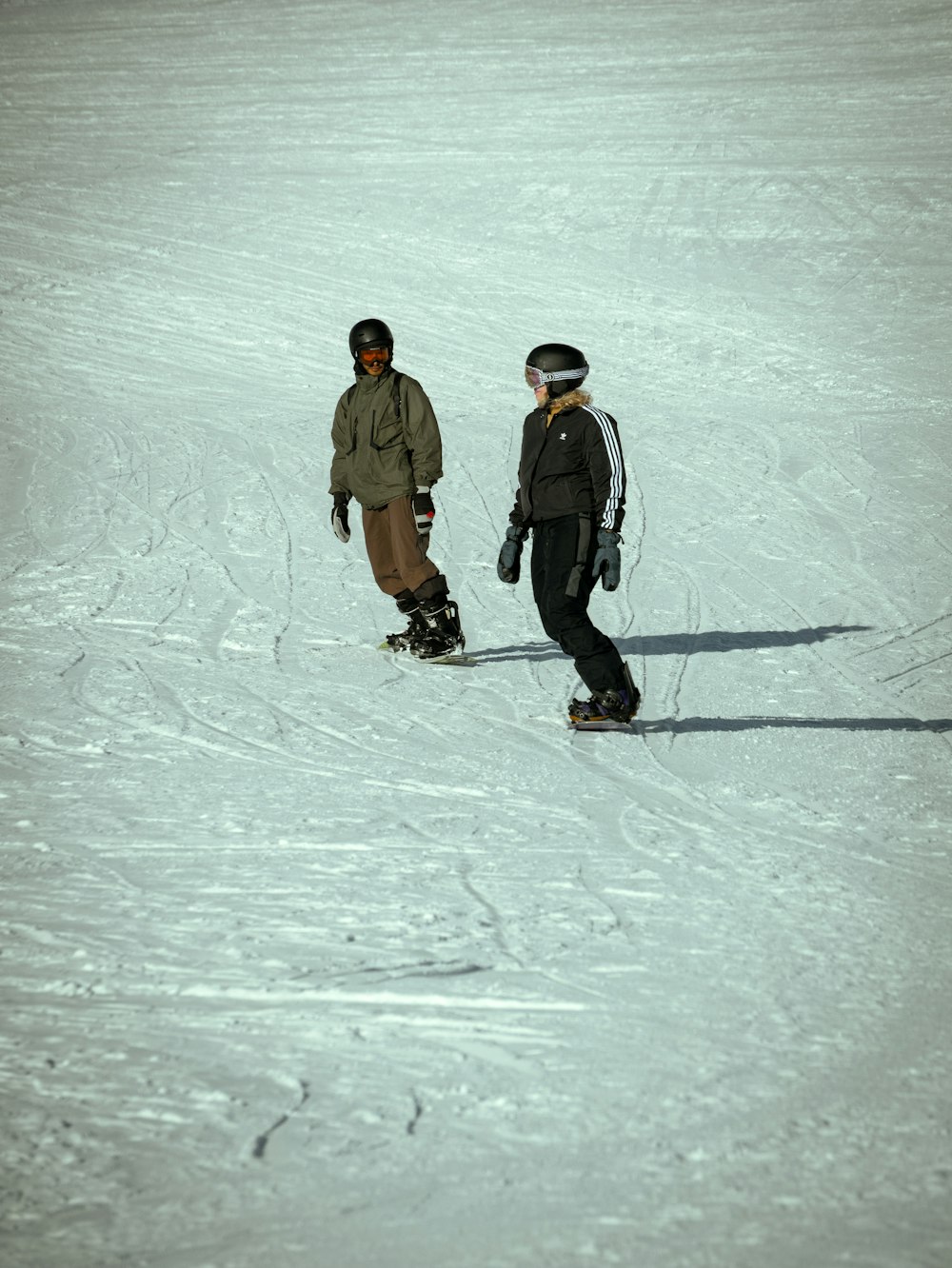 a couple of people riding snowboards down a snow covered slope