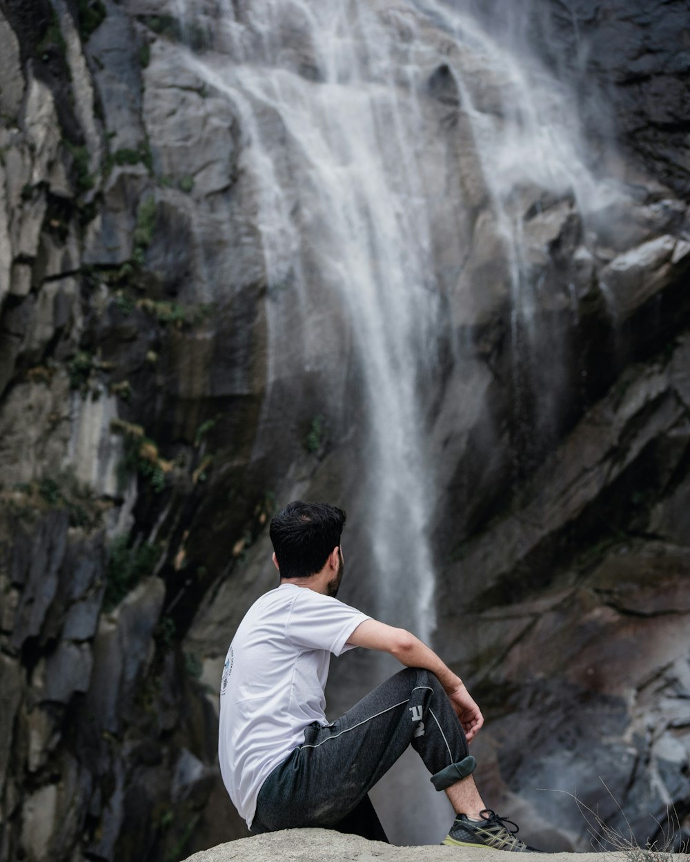 a man sitting on a rock in front of a waterfall