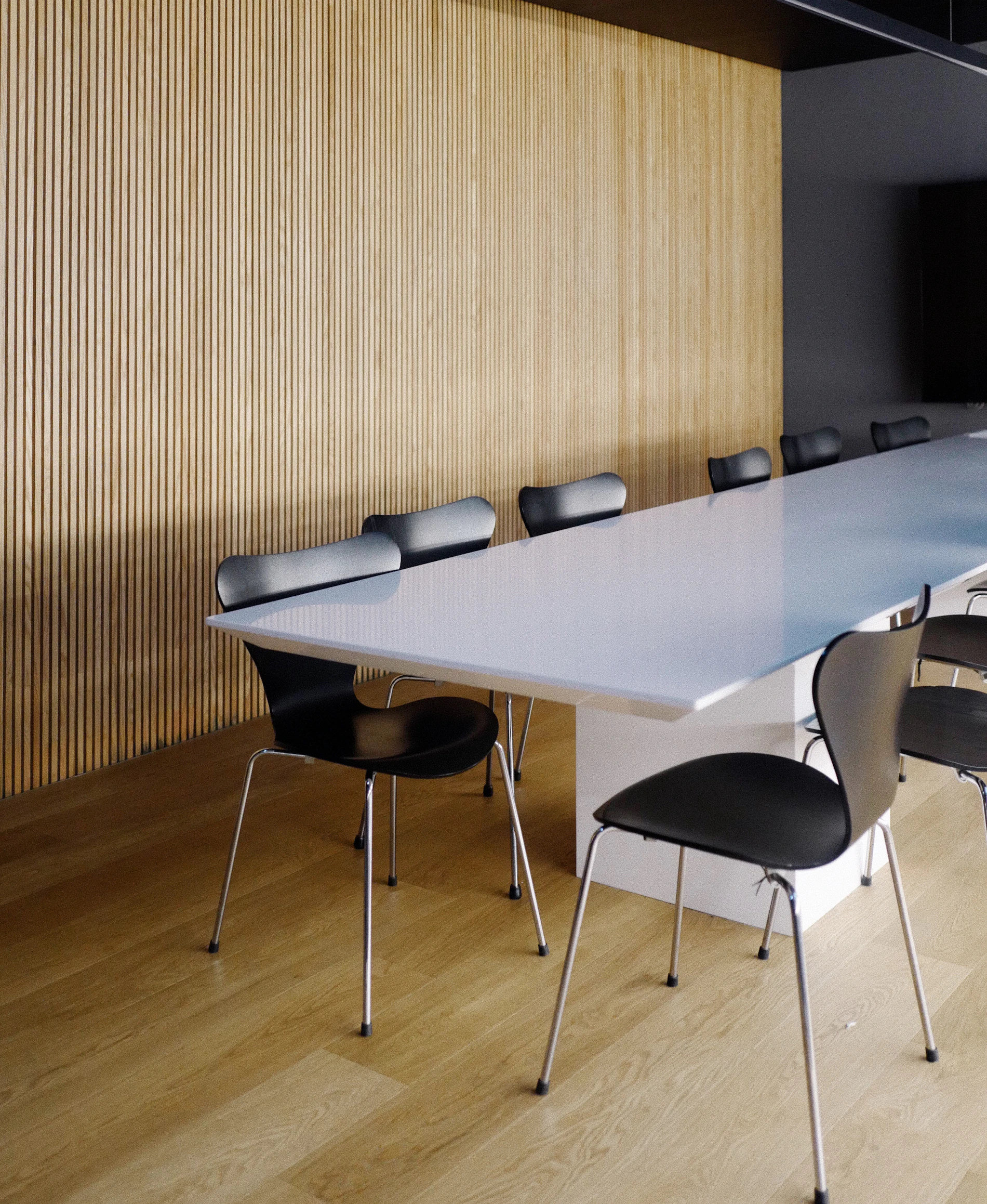 A long meeting table with chairs along one side, against a slatted wood wall