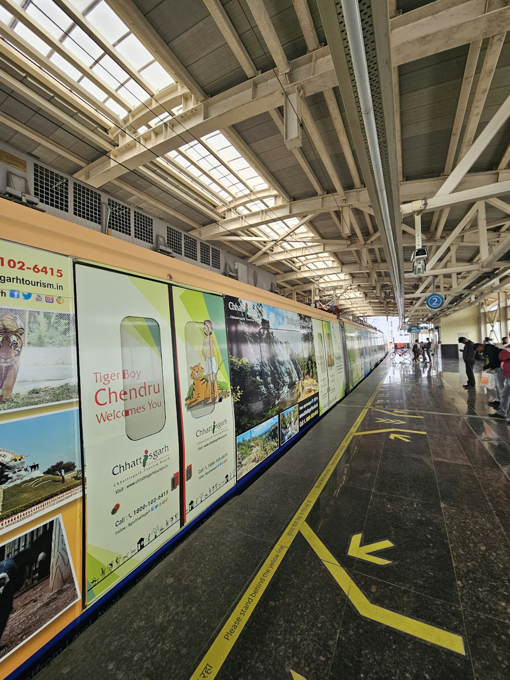 a train station with a long wall with advertisements on it