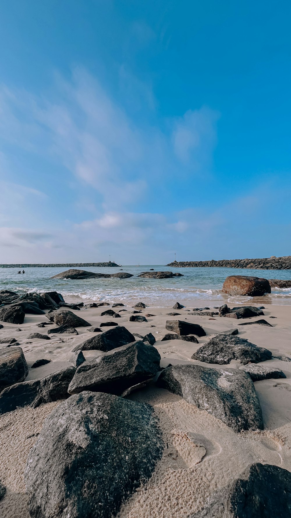 a sandy beach with rocks and water under a blue sky