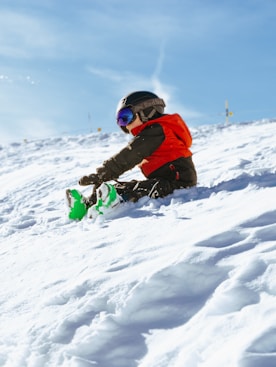 a young child sitting in the snow on a snowboard