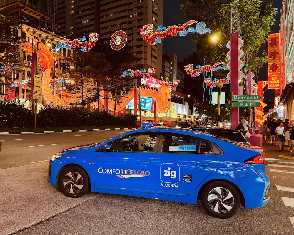 a blue car driving down a street next to tall buildings