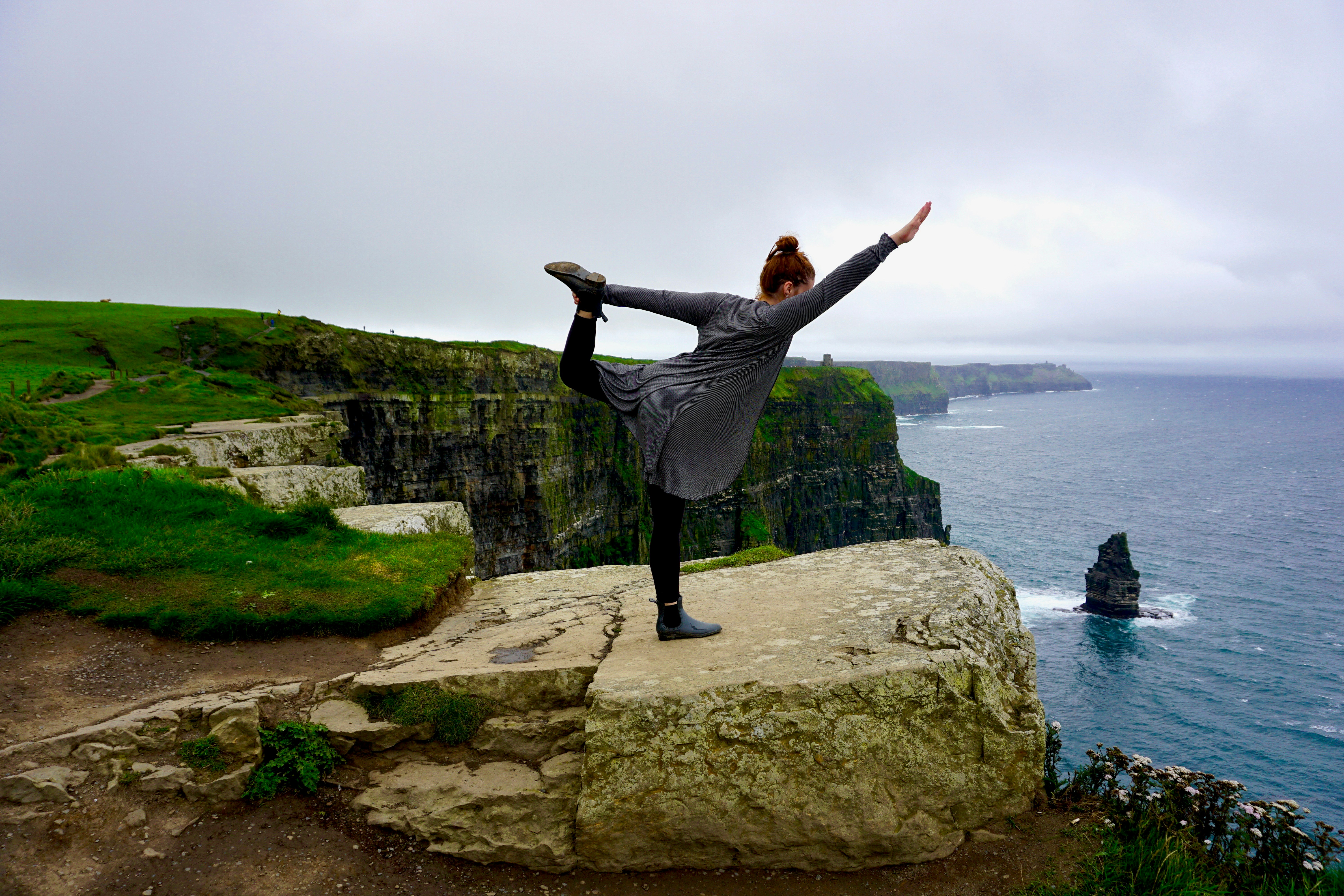 a woman doing a yoga pose on a cliff overlooking the ocean